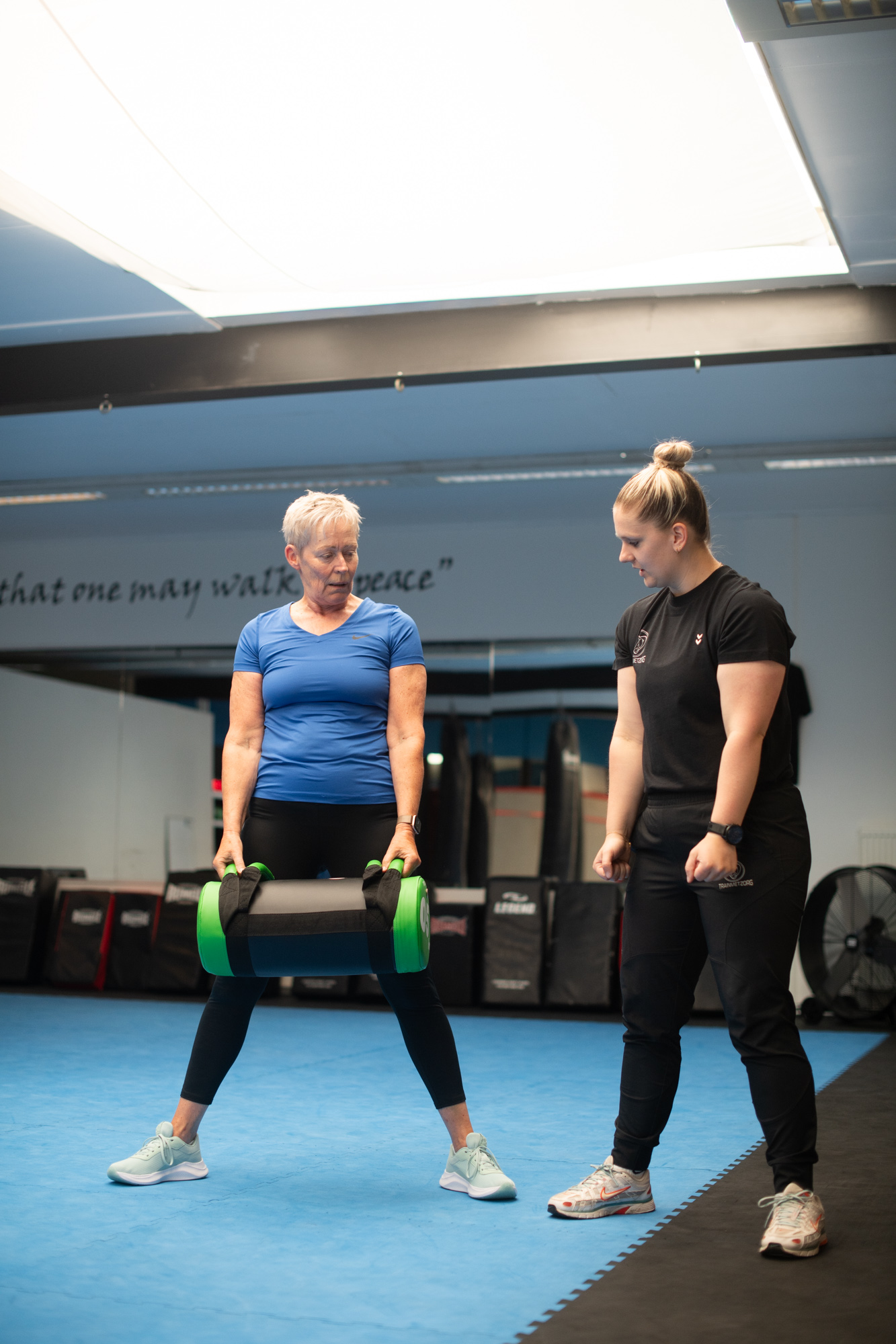 Esmee begeleidt een deelnemer bij een krachtoefening met een trainingsgewicht.